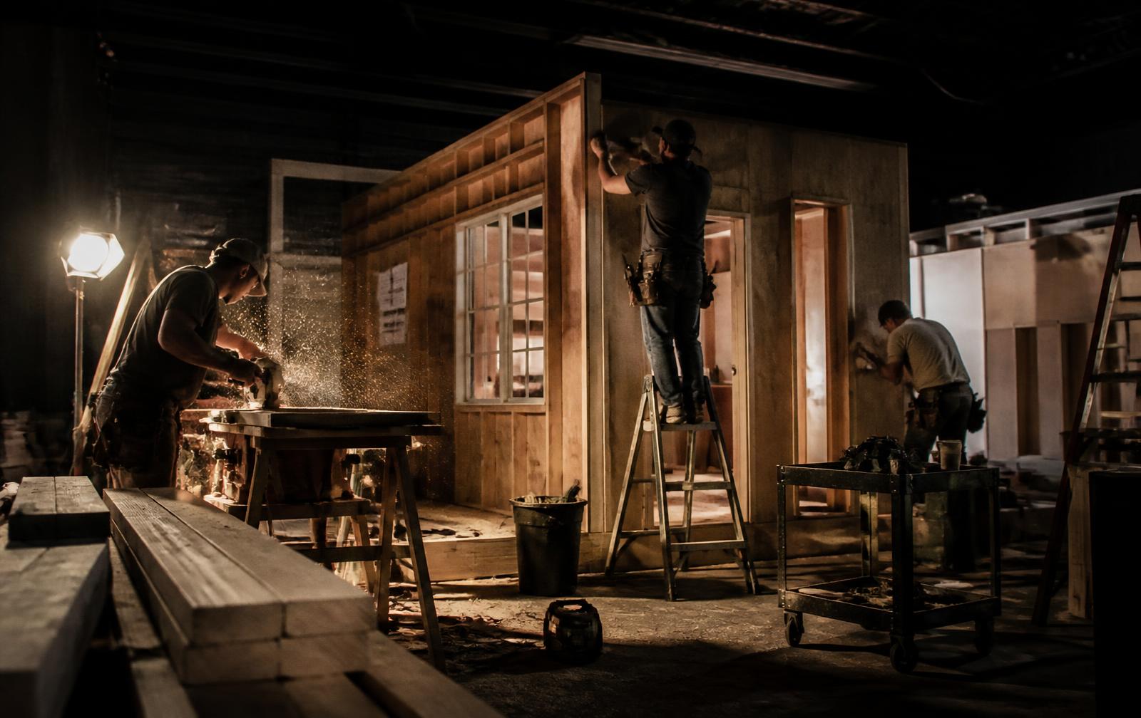 Set carpenters framing and finishing a wooden film set inside the warehouse